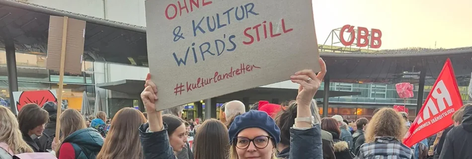 Landtagsabgeordnete Veronika Nitsche bei der Demo #kulturlandretten am Grazer Hauptbahnhof. Sie hält ein Schild: Ohne Kunst & Kultur wird's still.