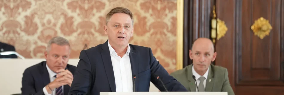 Landtagsabgeordneter Lambert Schönleitner am Rednerpult während einer Landtagssitzung. Im Hintergrund kann man Regierungsmitglieder erkennen.