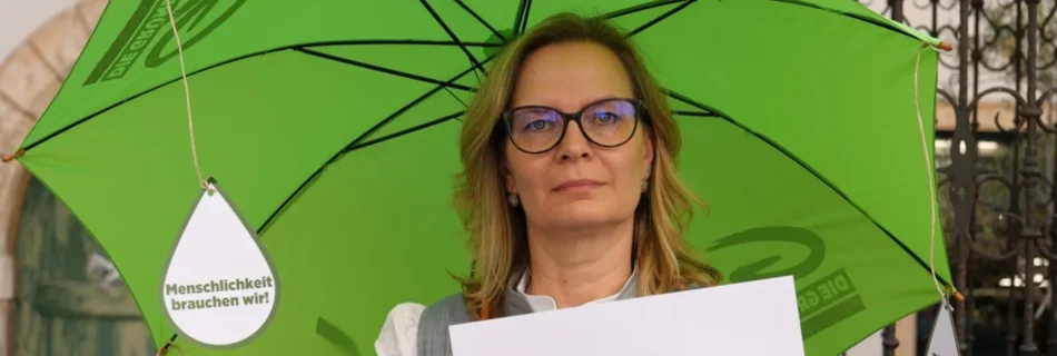 Landtagsabgeordnete Veronika Nitsche steht mit einem grünen Schirm (Rettungsschirm) und Demoschild #soziallandretten im Landhaushof