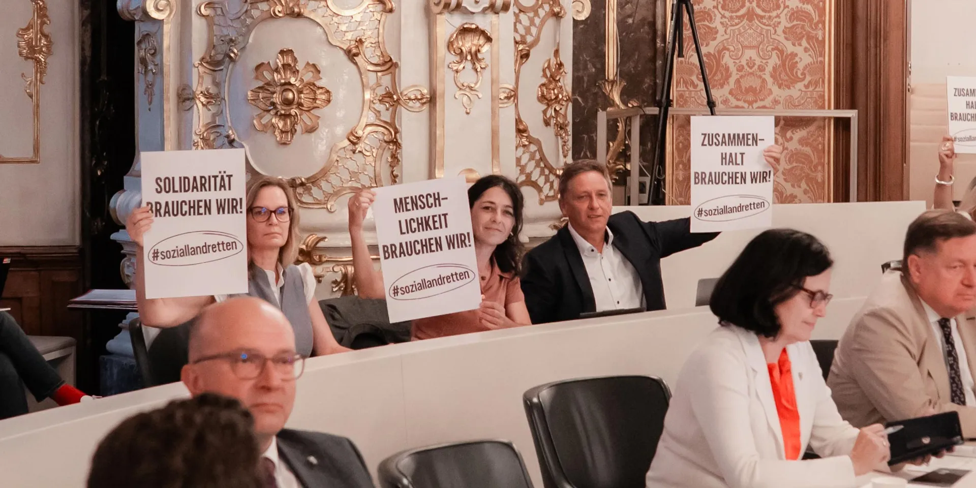Landtagsabgeordnete Nitsche, Krautwaschl und Schönleitner in der Landstube des Landhaus Graz (Sitzungssaal des Landtages) mit Schildern der Initiative #soziallandretten
