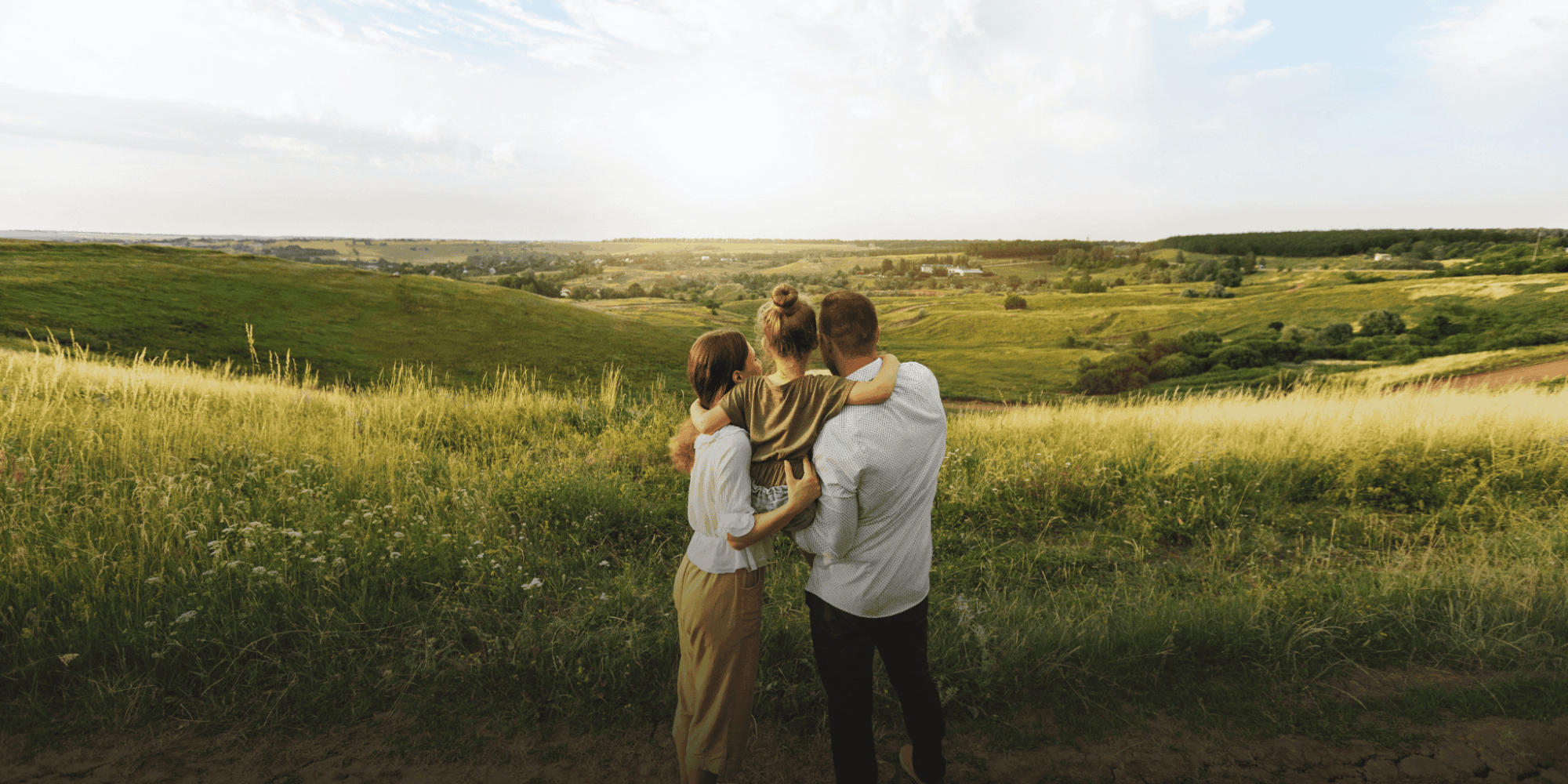 Zu sehen ist eine junge Familie vor einer grünen Wiesenlandschaft