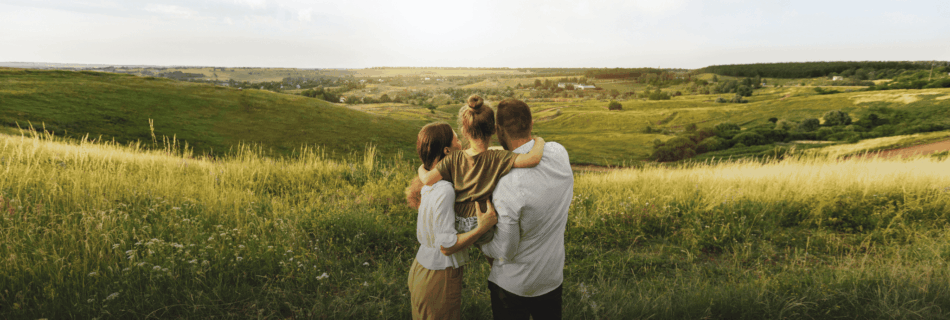 Zu sehen ist eine junge Familie vor einer grünen Wiesenlandschaft