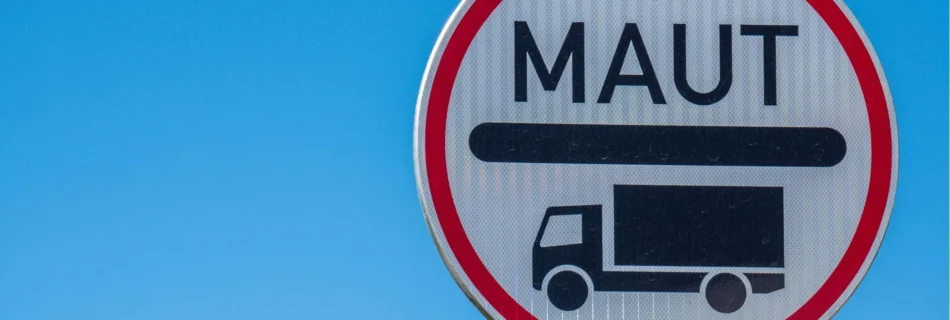 Ein rundes Verkehrsschild mit rotem Rand und der Aufschrift „MAUT“ über dem Symbol eines Lastwagens. Der Hintergrund ist ein klarer blauer Himmel.