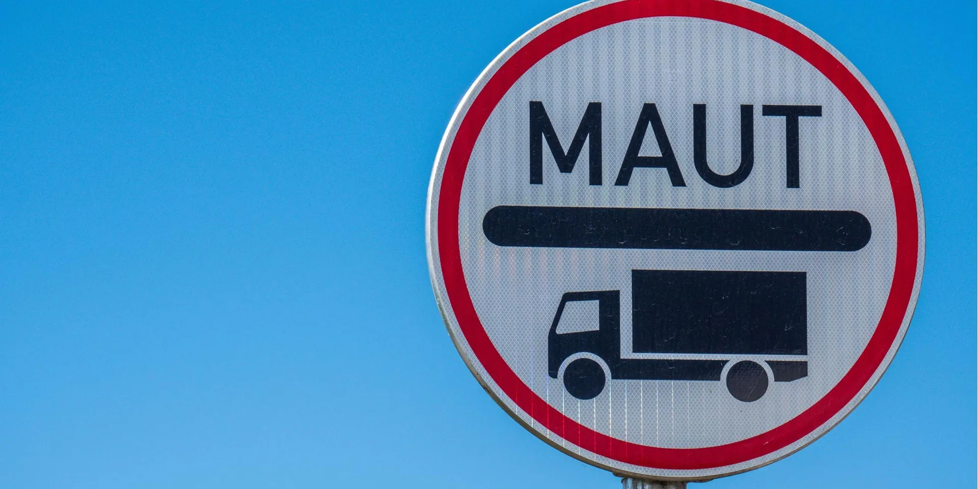 Ein rundes Verkehrsschild mit rotem Rand und der Aufschrift „MAUT“ über dem Symbol eines Lastwagens. Der Hintergrund ist ein klarer blauer Himmel.