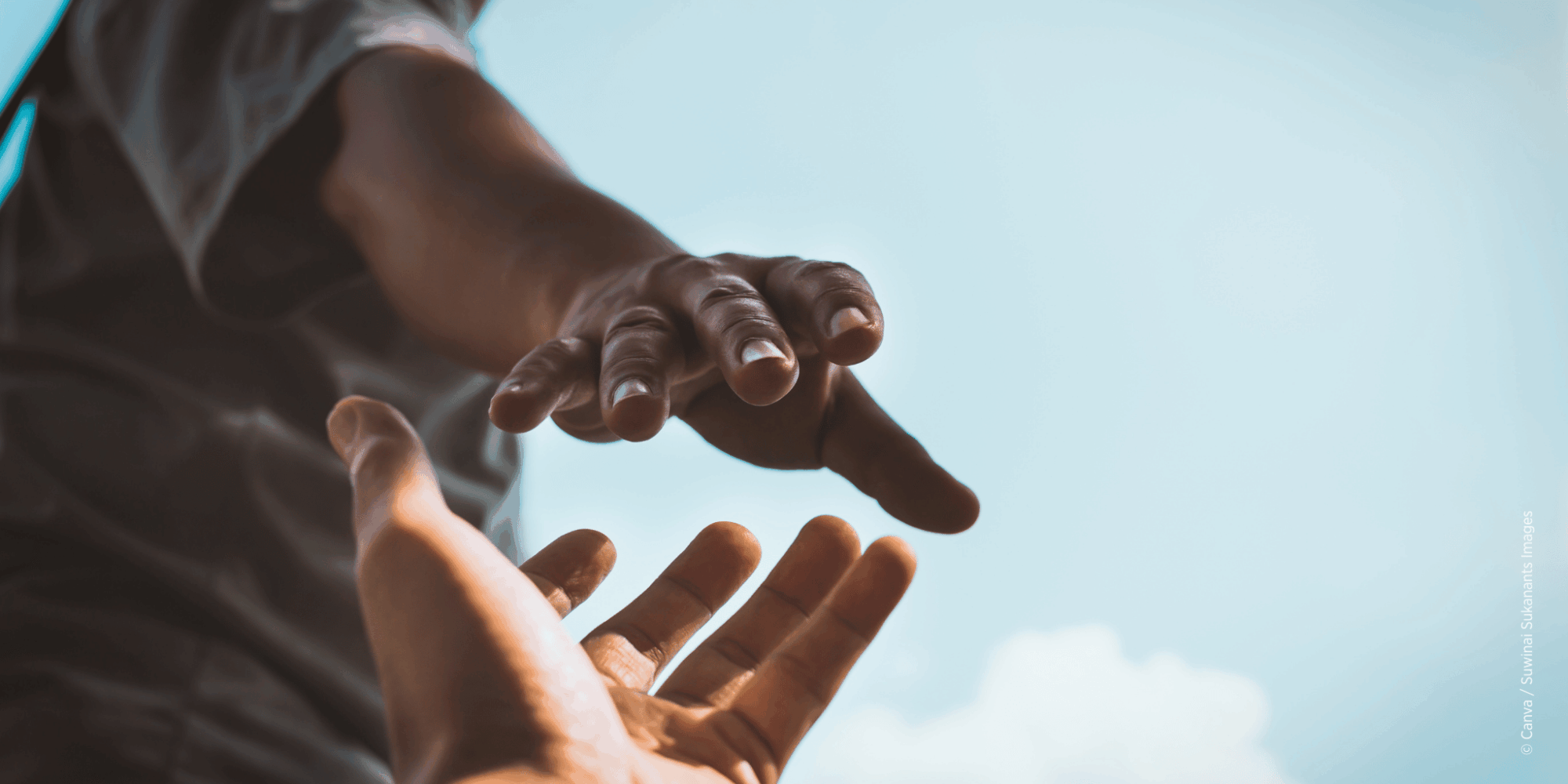 Eine Person reicht einer anderen Person die Hand. Blauer Himmel im Hintergrund.