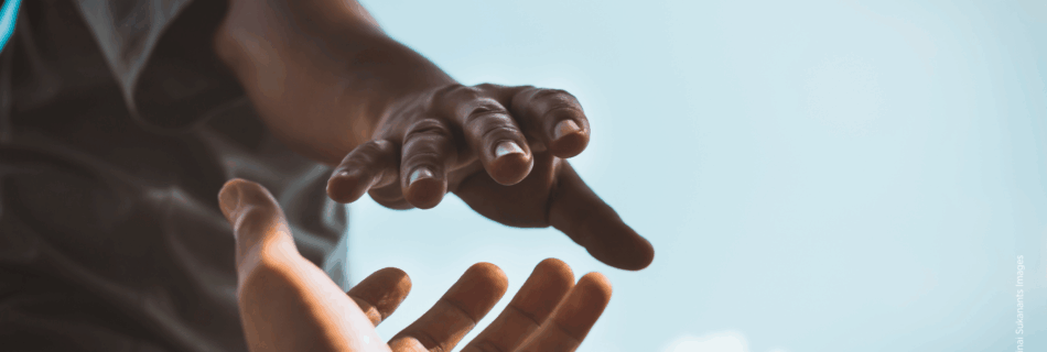 Eine Person reicht einer anderen Person die Hand. Blauer Himmel im Hintergrund.