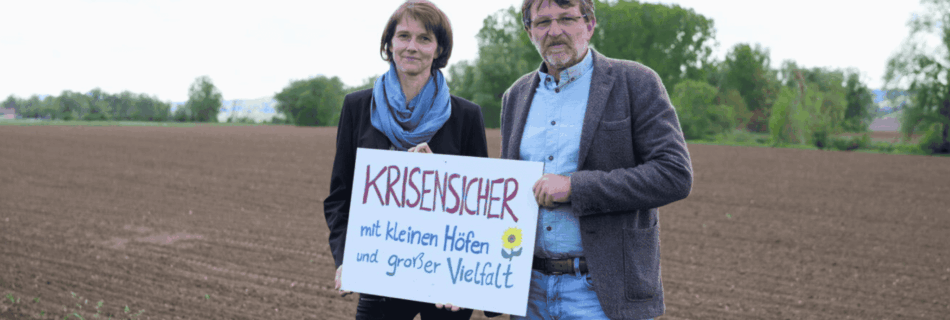 Katja Maurer und Andreas Lackner vor einem Feld mit einem Schild inder Hand: Krisensicher mit kleinen Höfen und großer Vielfalt