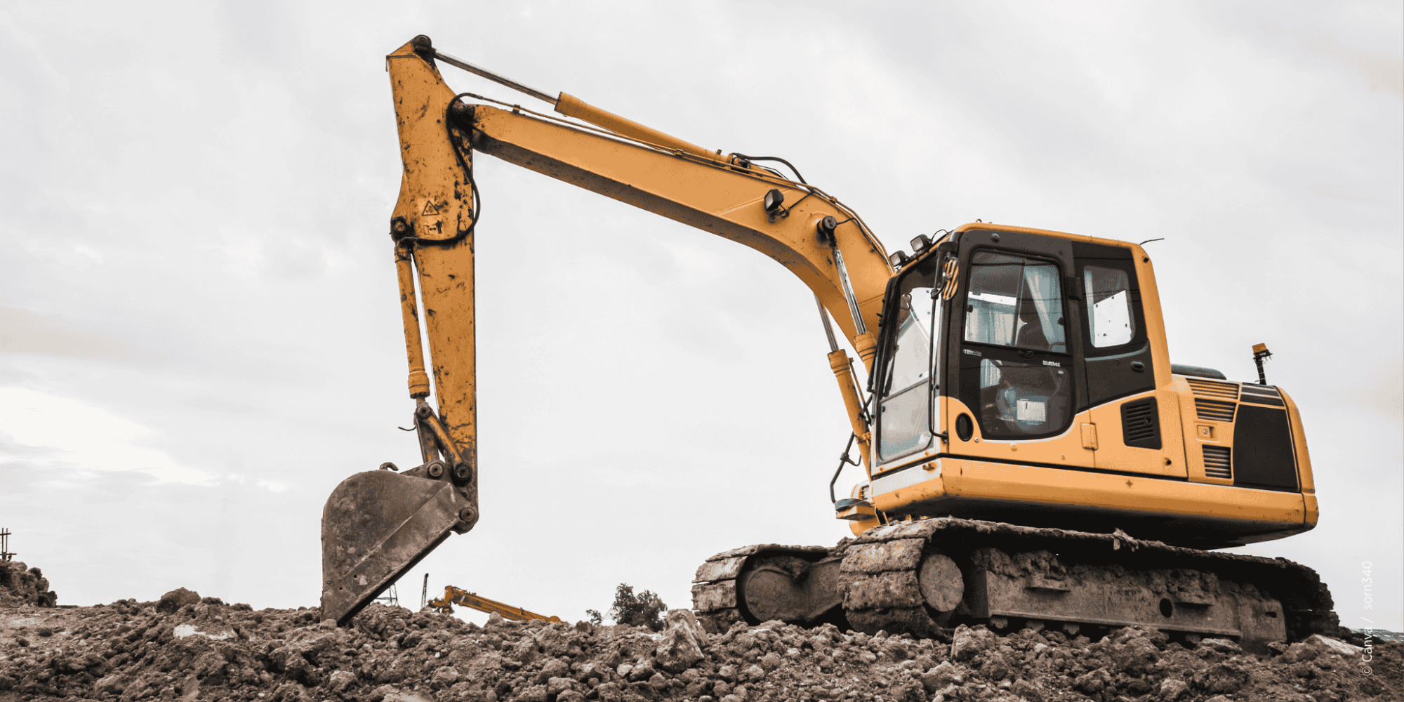 Gelber Bagger auf einer Baustelle bzw. Schotter mit Wolken bedecktem Himmel im Hintergrund