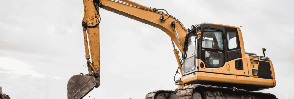Gelber Bagger auf einer Baustelle bzw. Schotter mit Wolken bedecktem Himmel im Hintergrund
